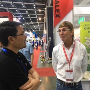 Two men stand smiling talking at a trade show.