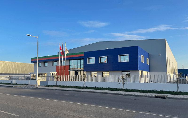 The front of the 90 Kenitra Morocco location building. Grey building with the second floor blue. Three flags hang in front of the building.