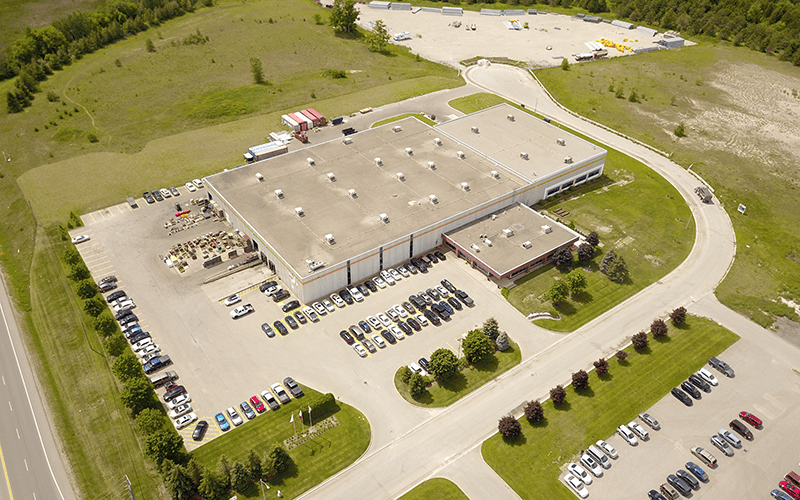 A areal view of the Uxbridge Canada building, with cars in the parking lot surrounded by green grass and trees.